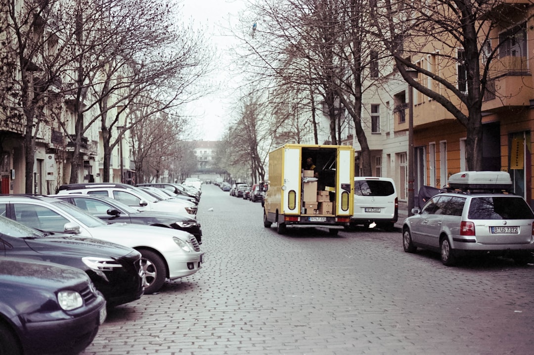 A street scene with parked cars and a delivery truck unloading boxes.